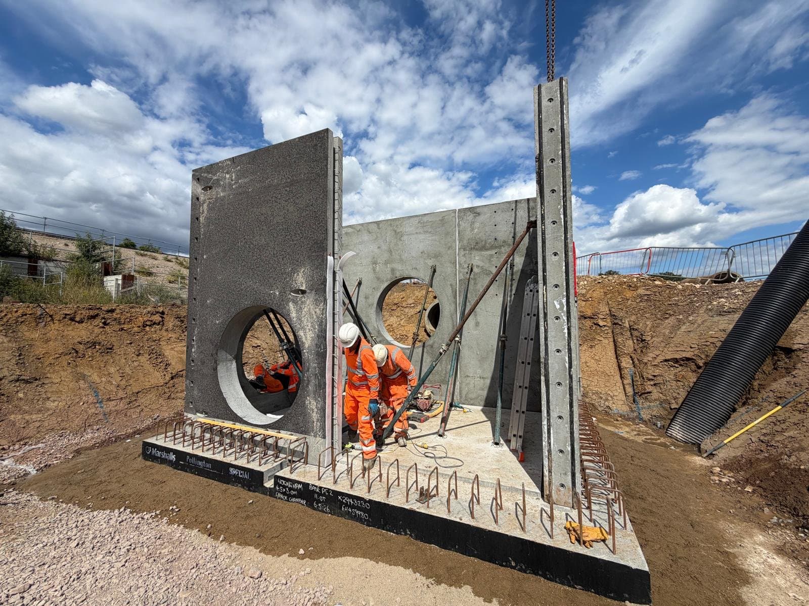 Marshalls Flat Pack manhole end wall panels braced by push-pull props while a side wall panel is lowered by crane