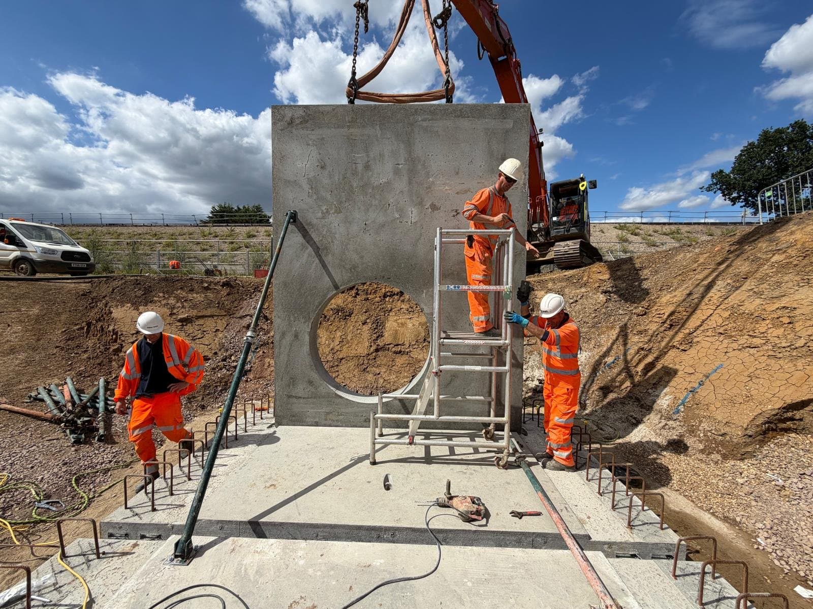 Precast end wall panel on the base slab with a raking push-pull prop and operatives on an access tower