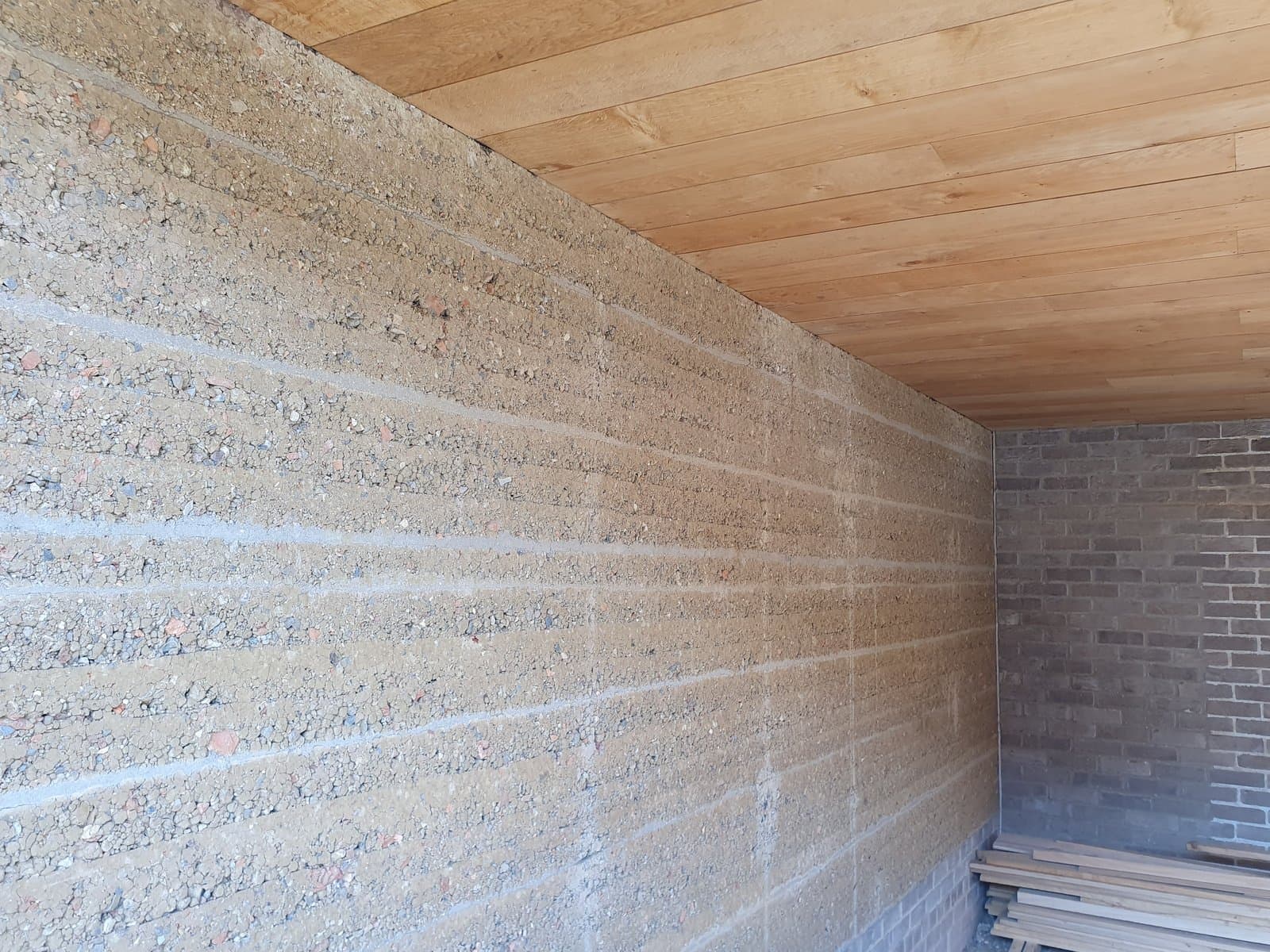 Rammed earth wall with its horizontal layer lines running to a brick return beneath an oak ceiling