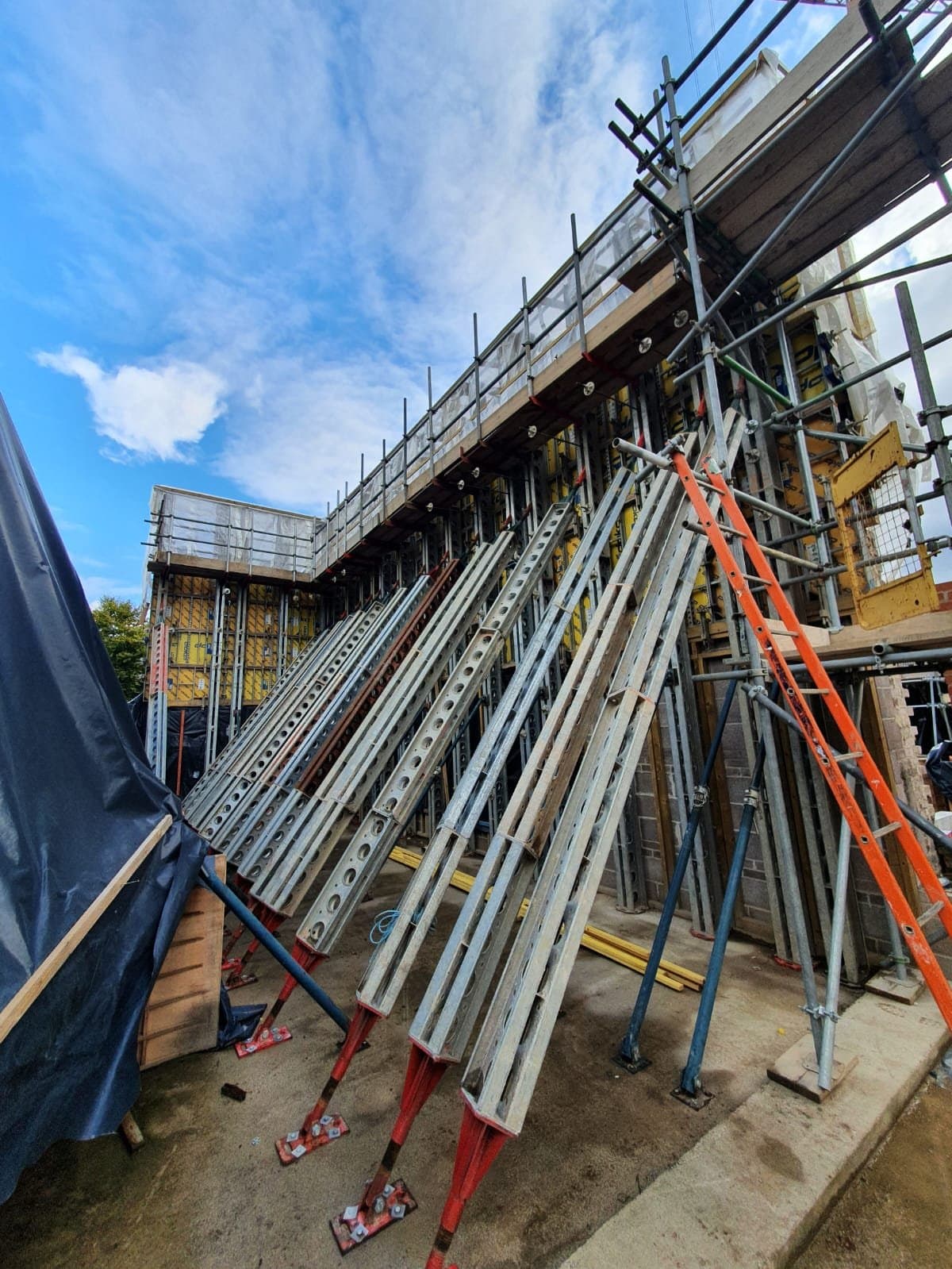 Slimshore raking shores on red base plates bracing the tall rammed earth formwork beside scaffolding