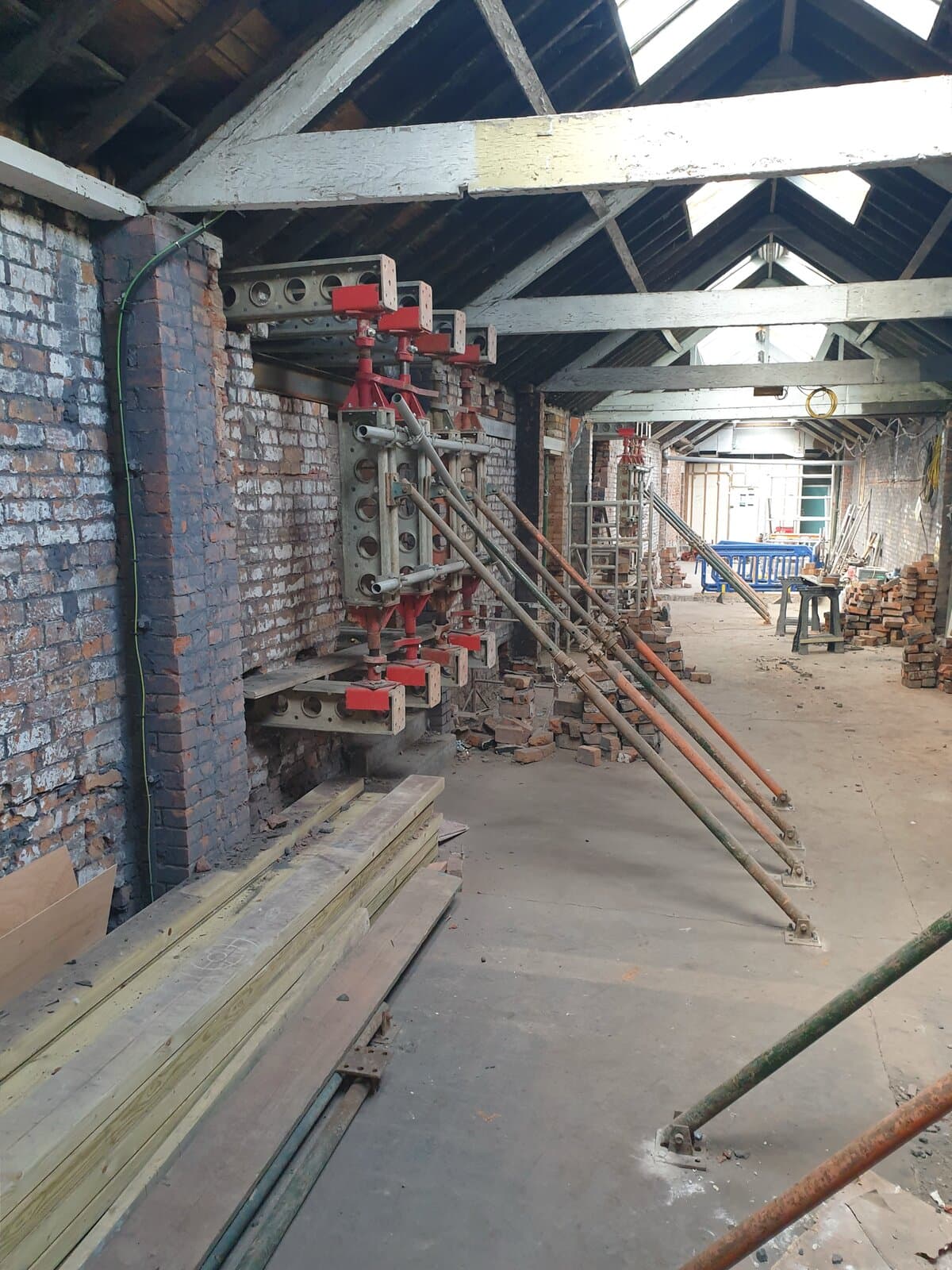 Slimshore reverse needling against a brick pier, braced by push-pull props, in a long room under the roof