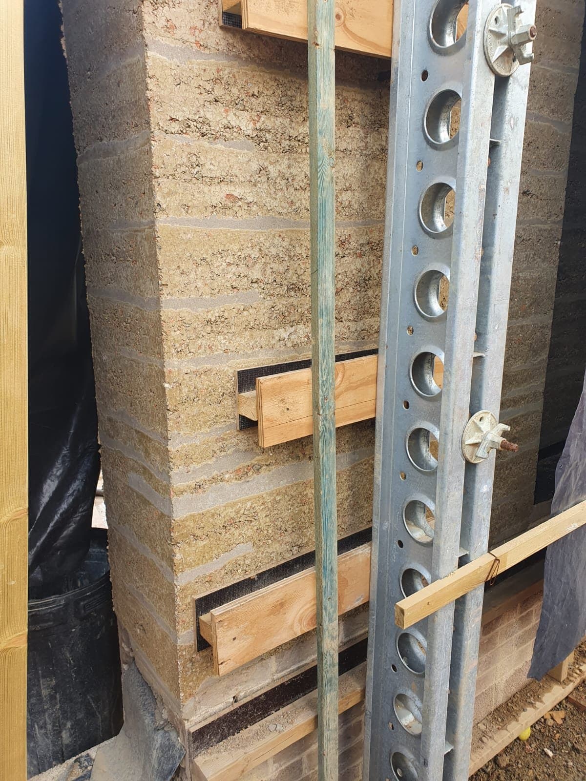 Close-up of a Slimshore soldier beside a rammed earth wall showing the compacted layer lines and timber ledgers