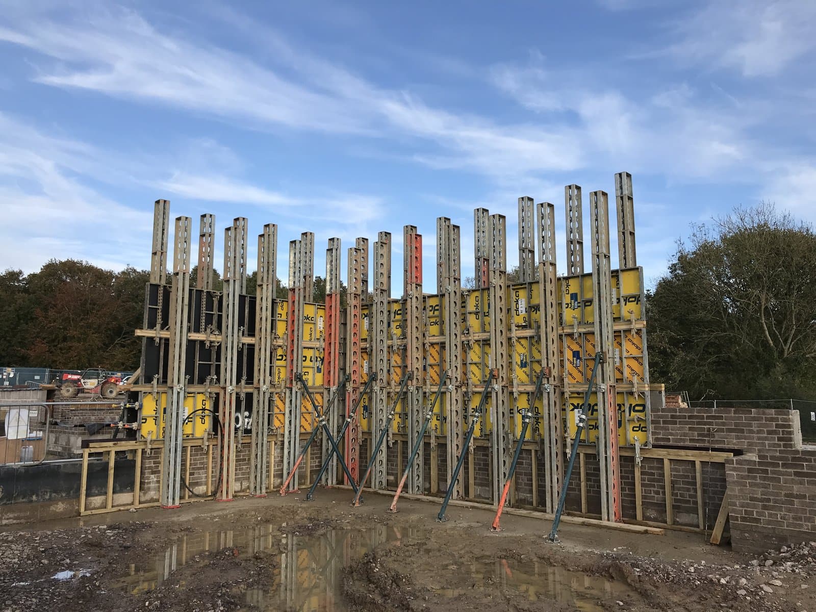 Doka Frami panels backed by a row of Slimshore soldiers and raking push-pull props on muddy ground at the start of the rammed earth walls