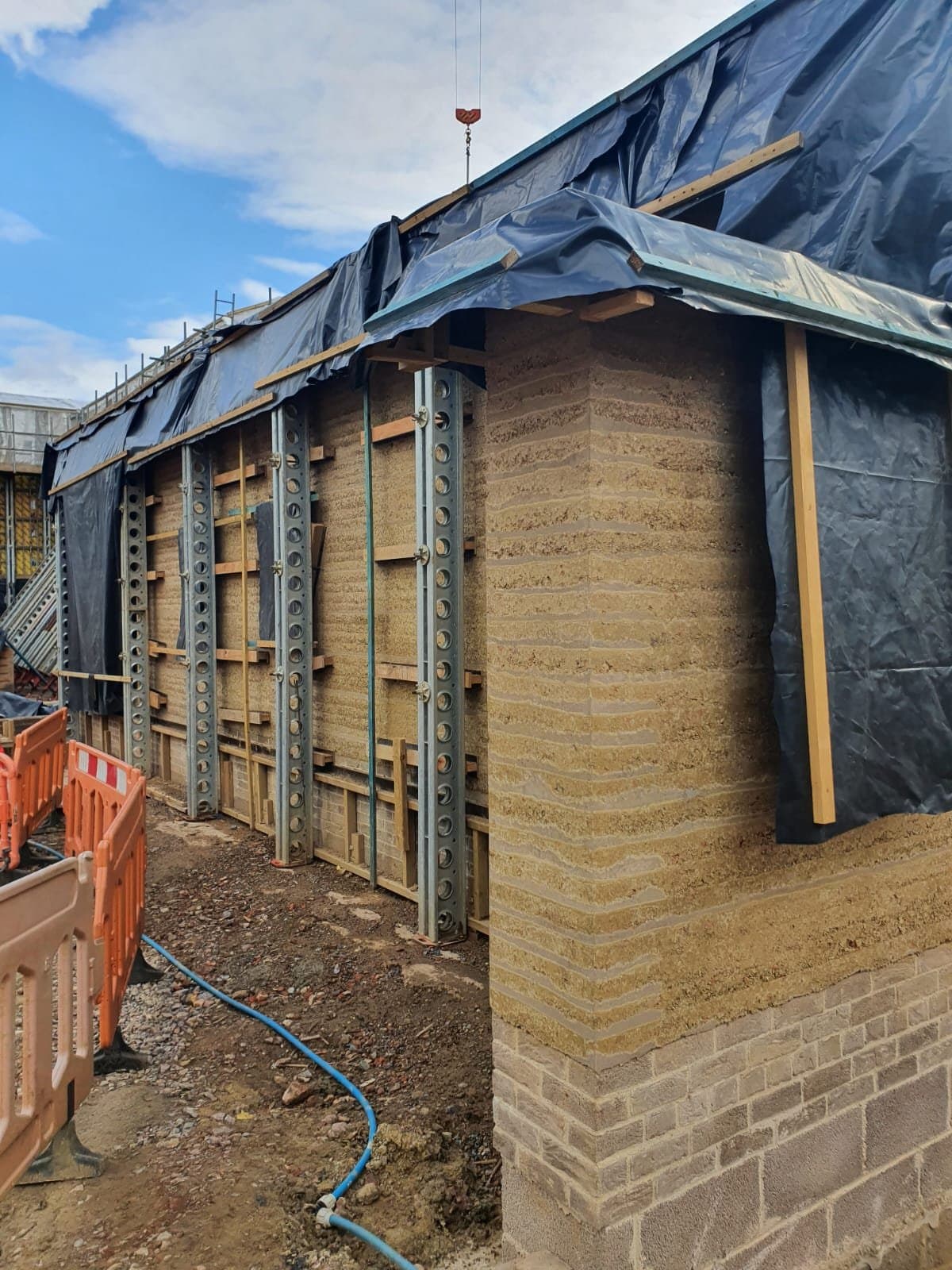 Slimshore soldiers against a rammed earth wall corner with black protective sheeting and timber bracing above