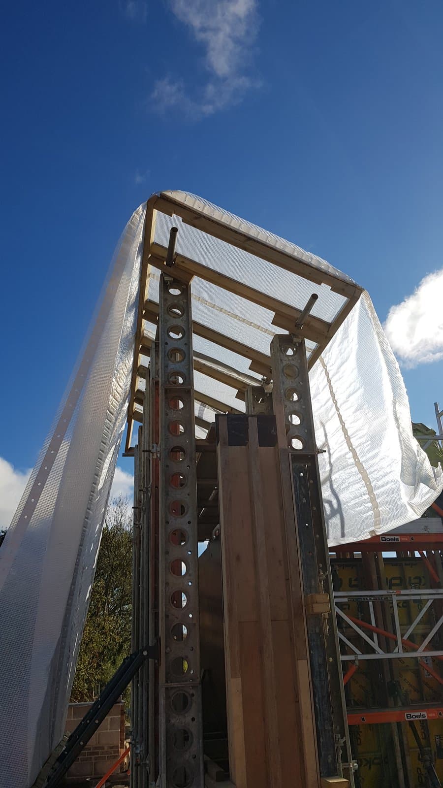 Looking up at Slimshore soldiers and a scaffold tube and sheeting weather-protection roof over the rammed earth formwork