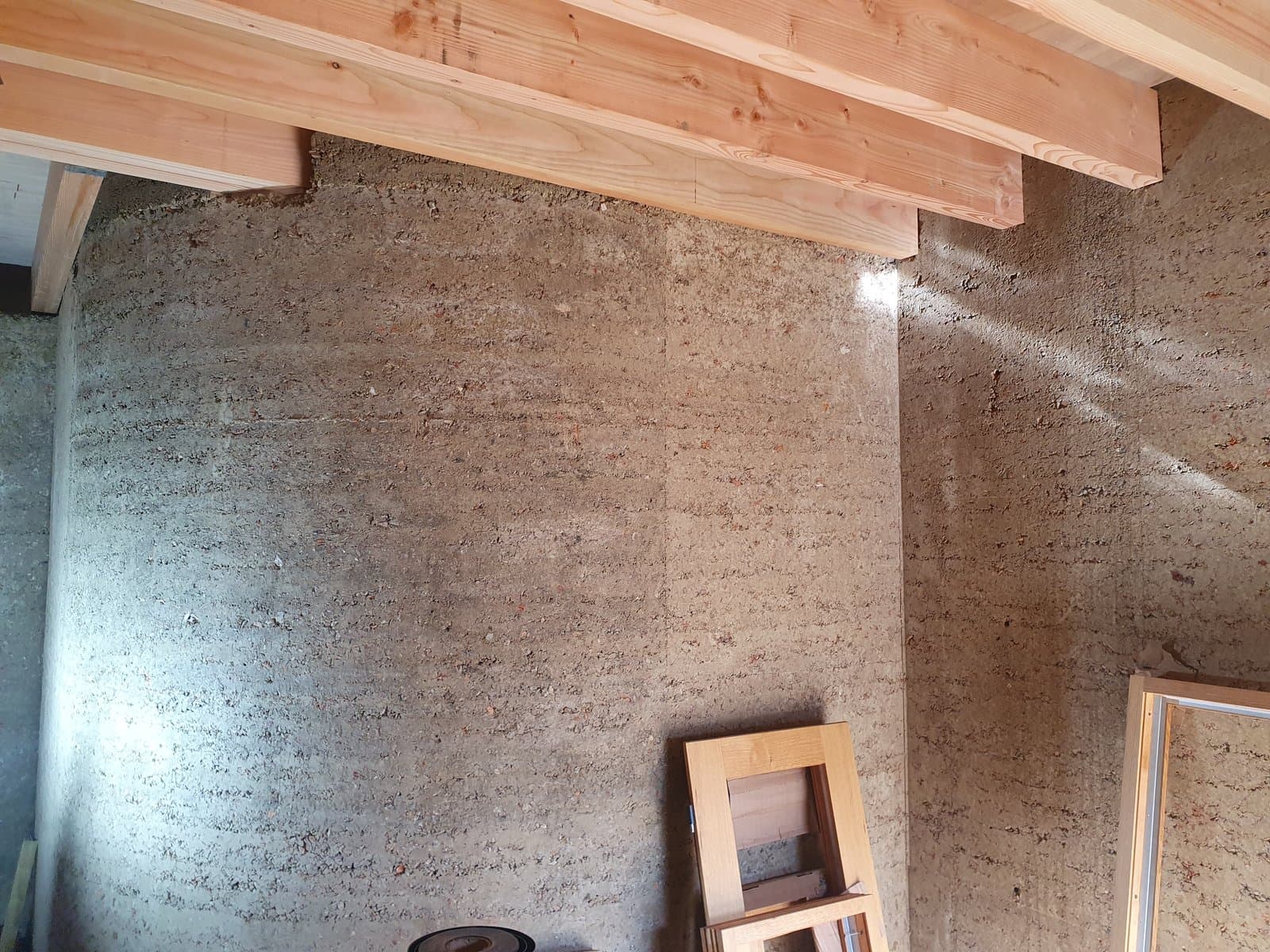 Finished curved rammed earth wall below timber beams inside the Rammed Earth House in Wiltshire